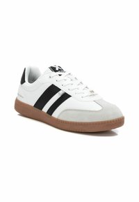 Zapatilla deportiva blanca con rayas negras, puntera de ante y suela de goma. Presenta cierre de cordones y detalles texturizados en la suela.