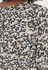 Tessuto leopardato in nero, beige e bianco, con dettaglio a chiave sulla schiena e texture morbida. Design casual e leggero.