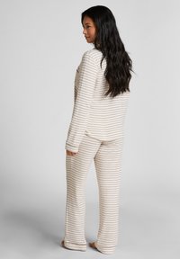 Gestreept pyjama set van zachte stof, bestaande uit een top met ronde hals en bijpassende broek met horizontale beige en lichtbruine strepen.