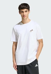 Biela bavlnená tričko s krátkymi rukávmi, na hrudi s malým hnedým grafickým dizajnom. Hladká textúra a bežný strih.