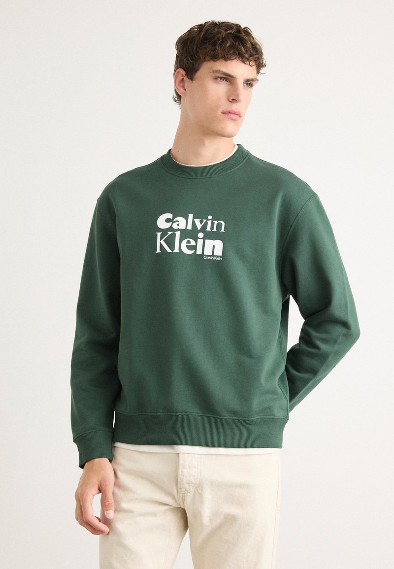Felpa verde a girocollo con logo bianco di Calvin Klein, realizzata in tessuto morbido con polsini e orlo a costine, vestibilità rilassata.