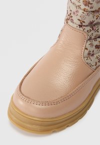 Részletes kép egy rózsaszín bőr csizmáról, gumitalppal és virágmintás textil gallér díszítéssel.