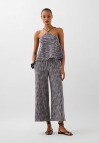 Top intrecciato multicolore con collo all'americana e orlo asimmetrico abbinato a pantaloni larghi con stessa fantasia. I sandali completano l'outfit.