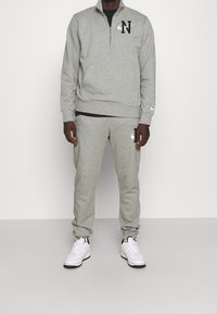 Szara bluza z pół-zamkiem i logo 'N'; zestawiona z dopasowanymi, szarymi dresami z logo Nike. Białe sneakersy dopełniają stylizację.