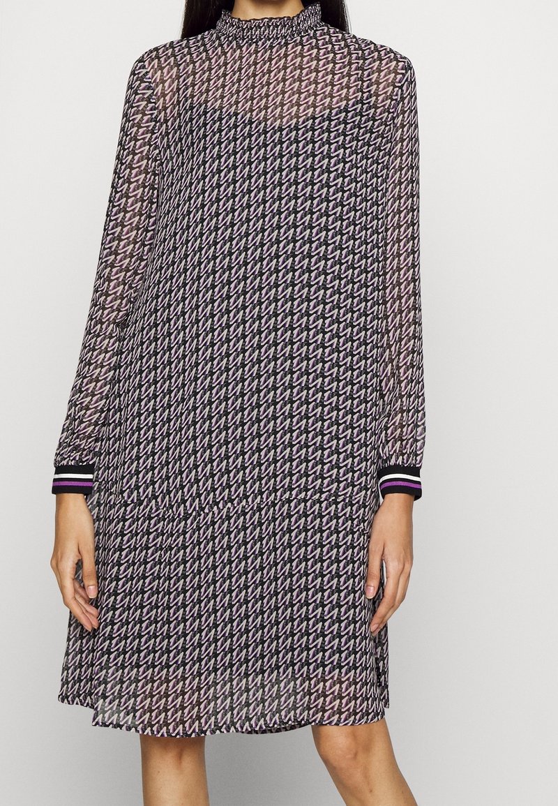 Langärmliges, durchscheinendes Kleid mit einem schwarz-lila geometrischen Muster, das einen hohen Kragen und gestreifte Ärmelabschlüsse in Schwarz, Lila und Pink aufweist.
