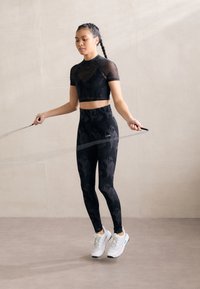 Zwarte gehaakte crop top met korte mouwen, gecombineerd met high-waisted legging met een tonale patroon. Witte sportieve schoenen met veters.