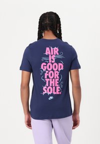 Tmavě modré bavlněné tričko s růžovým nápisem na zádech: "VZDUCH JE DOBRÝ PRO PODEŠEV," s obláčkovými motivy a malým logem Nike.