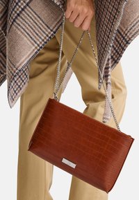 Borsa a tracolla in pelle marrone con embossing a forma di coccodrillo, forma rettangolare e una placca metallica con logo sulla parte anteriore.