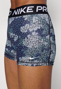 Szorty Nike Pro z niebiesko-szarym kwiatowym wzorem, elastycznym materiałem, kontrastowym szwem oraz czarnym pasem w talii z białym logo.