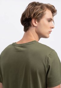 Olijfgroene katoenen t-shirt met een ronde hals en korte mouwen, voorzien van een subtiele geborduurde logo op de achterkant van de halslijn.