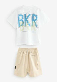 Ungdomsoutfit bestående af en hvid T-shirt med kortærmer med blå og grøn grafisk tekst "BKR" og beige shorts med sidelommer og logo.
