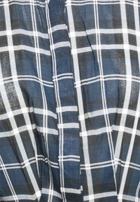 Camisa xadrez em azul-marinho e branco; tecido leve; apresenta um padrão de xadrez com diferentes larguras de riscas; textura suave; design casual.