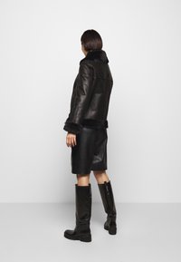 Svart läderjacka med fuskpäls i kragen och ärmsluten, matchad med en läderkjol och knähöga svarta stövlar. Slät textur, tajt passform.