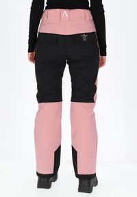 Pink and black ski pants with a high waist, side pockets, and reinforced cuffs. Features a textured fabric and a logo tag on the back.