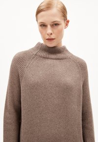 Braun gerippter Strickpullover mit hohem Kragen, der über eine strukturierte Oberfläche und verlängerte Ärmel verfügt, aus einem weichen, gemütlichen Material gefertigt.