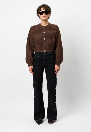 Brown knitted cropped cardigan with large buttons, paired with black flared jeans featuring button accents down the sides.