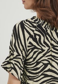 Blusa zebra a righe nera e crema con maniche corte a balza e scollatura arricciata, realizzata in un tessuto morbido e leggero.