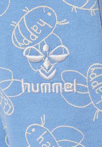 Ljusblått tyg med vitt broderat bi-mönster och ordet "hummel" i en stiliserad font, med en mjuk textur och lekfull design.