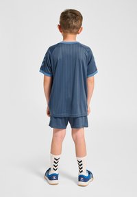 Dziecięcy strój sportowy w kolorze granatowym z pionowymi paskami, krótki rękaw, dopasowane spodenki oraz niebieskie tenisówki z białymi podeszwami i wzorzyste skarpetki.