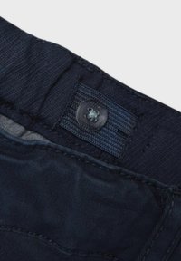 Tessuto blu navy con una texture liscia; presenta un bottone in plastica e una vita a bande con dettagli cuciti.
