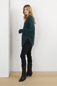 Poncho in teal lavorato a maglia con un motivo zigzag testurizzato, indossato sopra jeans neri attillati e abbinato a stivali cowboy neri alla caviglia.