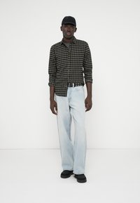 Fekete és zöld kockás, gombos ing, világoskék, széles szárú farmernadrág, fekete sapka, fekete cipő. Egyszerű kialakítás minimális díszítéssel.