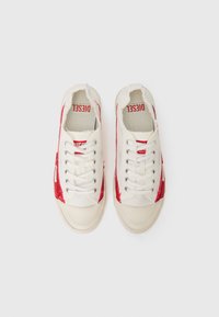 Tenisi din pânză în off-white cu accente roșii. Prezintă un design low-top și o talpă din cauciuc texturată. Detalii stilizate în jurul marginilor.