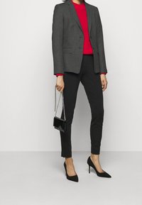 Grå skræddersyet blazer over en rød ribbet sweater, parret med sorte tætsiddende bukser og sorte spidse hæle. Accessoriseret med en lille sort taske.