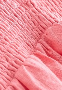 Pink tekstil med en struktureret, sammensat design med fremtrædende plisseringsdetaljer. Blødt, let materiale med en glat overflade.