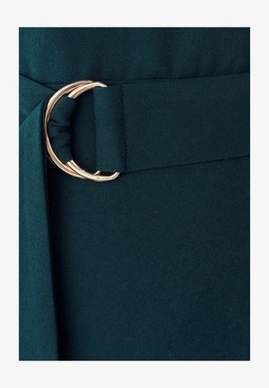 Modrozelená látka s preloženou časťou so zlatým kovovým okrúhlym prackou, vytvárajúca hladkú textúru a štruktúrovaný dizajn.