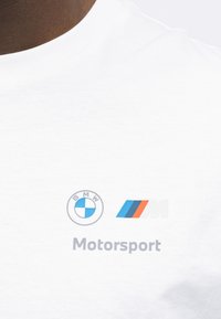 Λευκό πουκάμισο με το λογότυπο BMW roundel, το λογότυπο με τις τρισχρωμικές ρίγες M και τη λέξη "Motorsport" τυπωμένη στο στήθος.