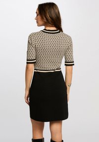 Knit dress featuring a beige top with a repeated black letter 'M' pattern and a solid black skirt. Short sleeves and contrasting trim details.