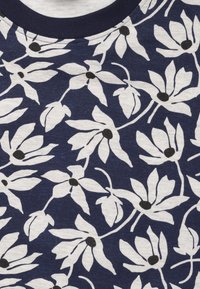 Navyblauwe stof met een wit bloemenpatroon met zwarte centra. Katoenen textuur, ronde halslijn met een contrasterende donkerblauwe rand.