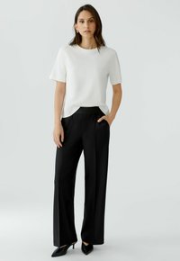 White short-sleeve t-shirt paired with black loose-fit trousers featuring a smooth texture and a wide leg design, complemented by pointed black heels.