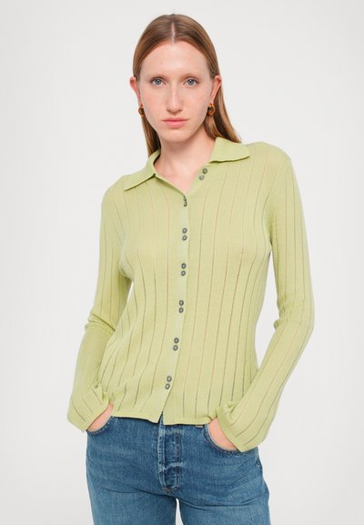 Svetlo zelena rebrasta jopica z ovratnikom, sprednjim zapenjanjem na gumbe in dolgimi rokavi; vsebuje subtilne navpične črte in sive gumbe.