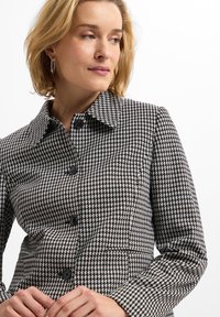 Black and white houndstooth patterned jacket features a structured collar and buttons, with a tailored fit and side pockets.