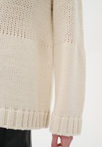 Kraftig strikket cremet sweater med ribbede manchetter og kant. Har kontrasterende strikkemønstre og en hyggelig, struktureret finish.