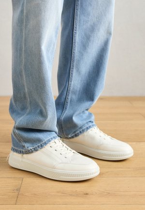 Valged nahast tennisekotid madala ülaosaga disainiga, tekstuursete aktsentidega ja ümmarguste varvastega, millele on kombineeritud helesinised denim jeans.