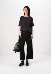 Svart strikket topp med korte ermer, parret med vide svarte bukser. Modellen bærer en svart skinnveske og har på seg svarte blokkhelte sko.