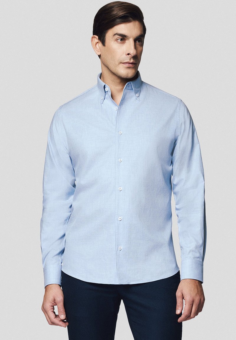 Jasnoniebieska koszula na guzik wykonana z miękkiego materiału, z klasycznym kołnierzykiem, długimi rękawami i białymi guzikami. Gładka tekstura bez wzorów.