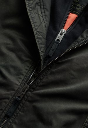Black bomber jacket with a matte finish, featuring a contrasting orange lining, two zippers, and a textured fabric. Quilted details visible.