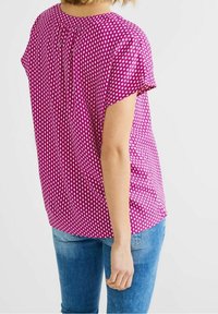 Kortärmad topp i rosa med ett geometriskt mönster, med rundad halsringning och plisseringar på baksidan. Matchas med blå jeans.