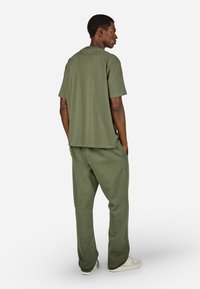Olivová zelená voľná tričko a zodpovedajúce tepláky, s hladkou textúrou, okrúhlym výstrihom a bočnými vreckami, doplnené svetlými teniskami.