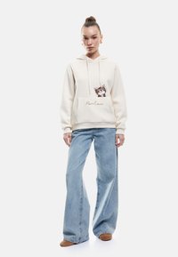 Sudadera crema con un gráfico de un gato y el texto "PurrLave", combinada con jeans de pierna ancha de tiro alto en azul claro. Tejido suave, ajuste casual.