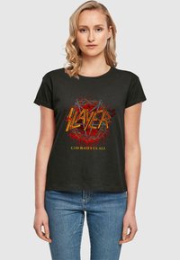 Sort bomulds t-shirt med korte ærmer, prydet med en livlig grafik: "SLAYER" i gul og rød, med "GOD HATES US ALL" nedenfor i gul.