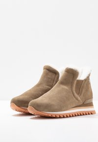 Bottines en suede marron avec une doublure en fausse fourrure blanche, des panneaux latéraux élastiques et une semelle en caoutchouc texturée présentant un motif en zigzag.