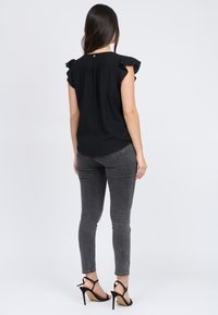Top nero con maniche a volant, tessuto strutturato e orlo curvo. Abbinato a jeans skinny grigi e sandali neri con tacco alto.