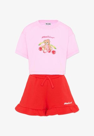 T-shirt courte rose avec motif d'ours en peluche et cerises, associée à un short rouge à cordon avec ourlet à volants et logo Moschino.