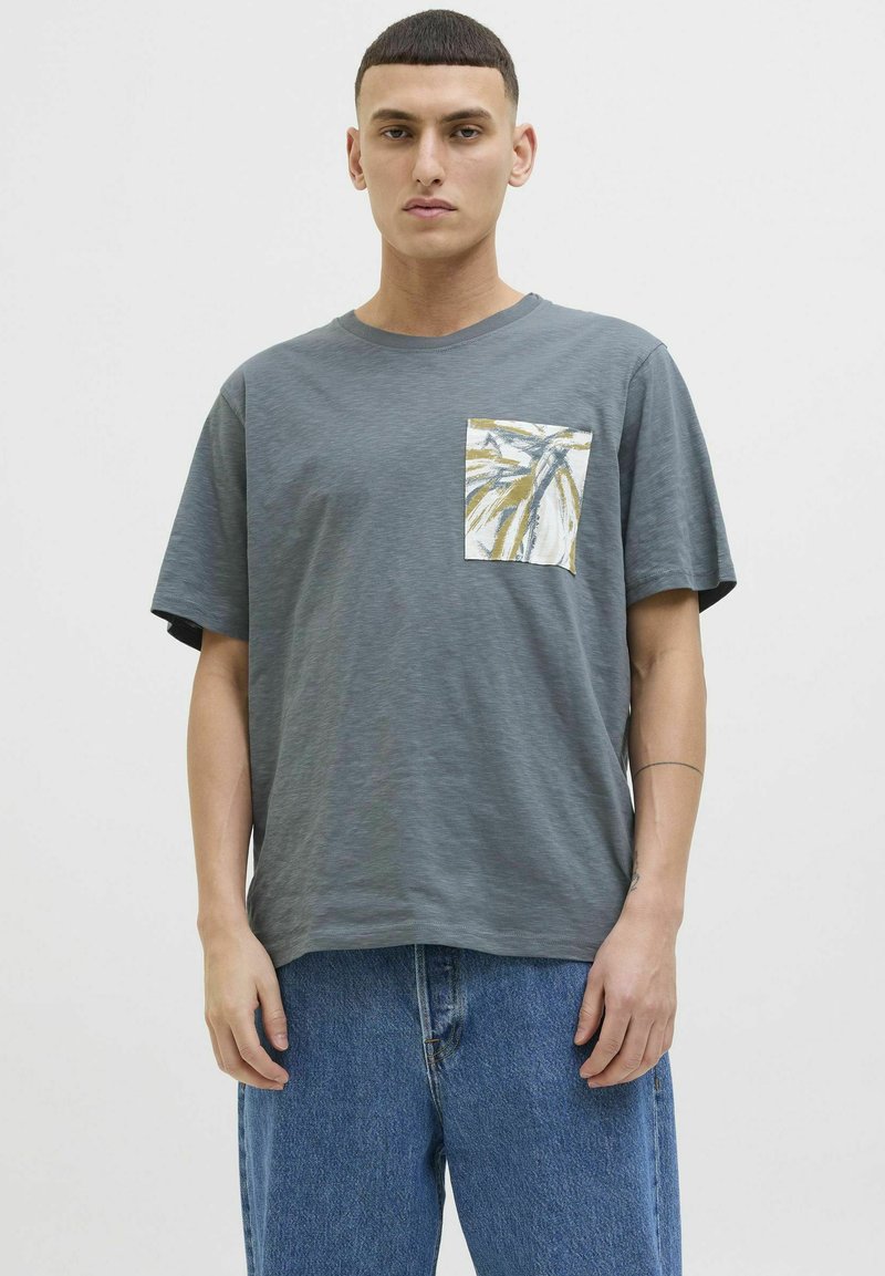 Camiseta gris de manga corta con una textura especial, que presenta un bolsillo en la parte delantera de color blanco decorado con un diseño de hojas amarillas y verdes.