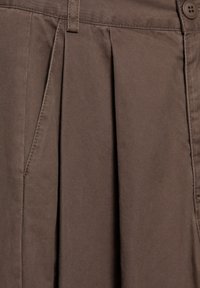 Bruin geplooid textiel met een gladde textuur, voorzien van een zijzak en een knoopdetail op de tailleband.